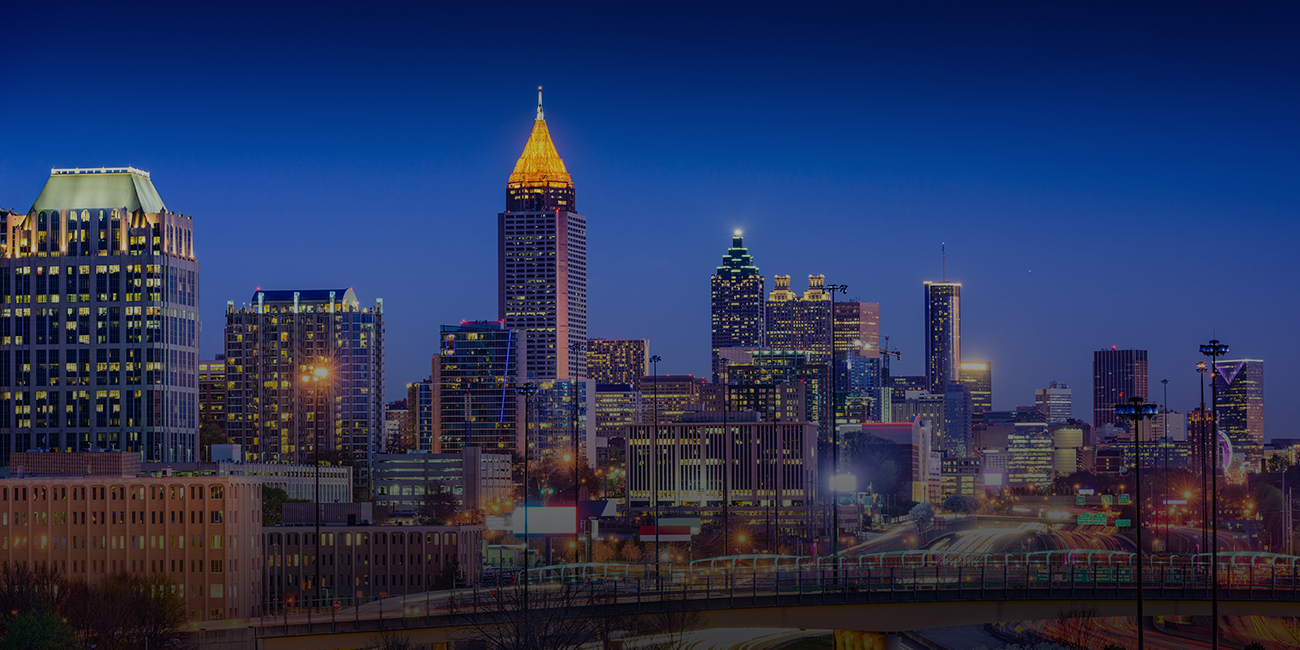 Nighttime skyline view of a brightly lit city with tall buildings and a clear sky.
